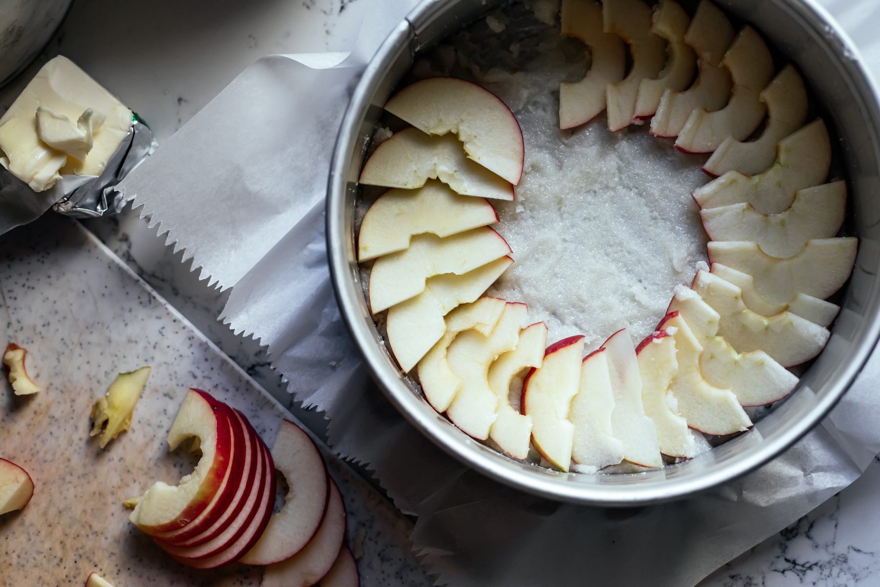 פרוסות תפוחים מסודרות כמניפה בתחתית תבנית עגולה הכנת עוגת פרג שקדים ותפוחים הפוכה-שני סנדרס